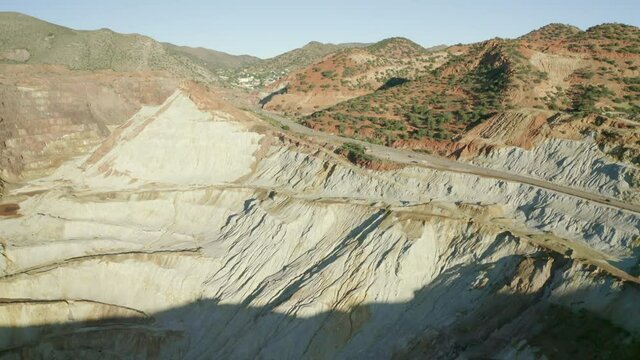 Aerial shot of vehicles on road by copper mine during sunny day, drone flying forward over quarry against mountains - Bisbee, Arizona