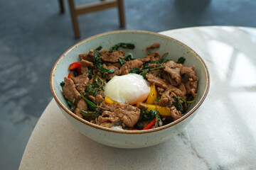 Close up bowl of Pad Kaprow, stir fry holy basil leaves with beef and poached egg served on rice- Classic Thai recipe