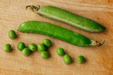 Green fresh pea pods and peas on wooden background, top view