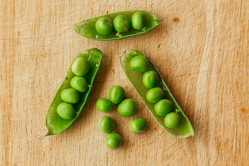 Green fresh pea pods and peas on wooden background, top view