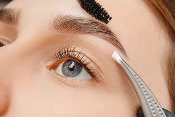 Fotobehang Master tweezers depilation of eyebrow hair in women, brow correction © Parilov