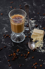 a cup of latte on a black background with pieces of white chocolate
