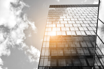 Facade texture of a glass mirrored office building. Fragment of the facade. Bottom view of modern skyscrapers in business district in evening light at sunset with lens flare filter effect. Black and w