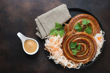 Roasted coiled pork sausages with sauerkraut and mustard over dark brown metal background, top view with copyspace, horizontal shot