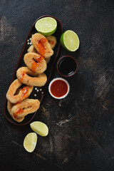Roasted panko breaded calamari rings with limes and dips, vertical shot on a dark brown stone background, top view, copyspace