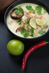 Close-up of tom kha or thai coconut milk and chicken soup served in a black bowl, vertical shot on a black stone surface