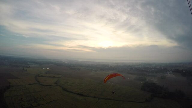 Person on motorized parachute as adrenaline and extreme sport activity falling from sky with open fileds and mountaind at the background. Pilot man on the paraglider point of view shot.