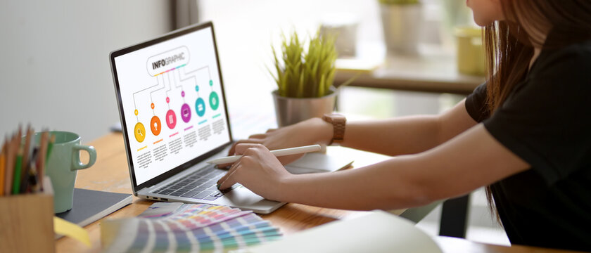 Female graphic designer concentrating on her project with laptop and other supplies on worktable