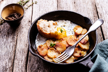 Fried Eggs and Potatoes in cast iron skillet on rustic wooden table. Skillet Breakfast. Selective focus