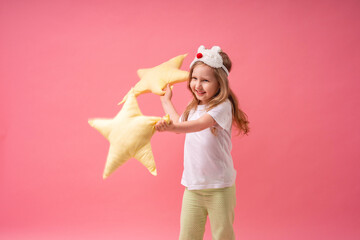 An adorable little girl in a sleep mask and pyjamas is holding pillows