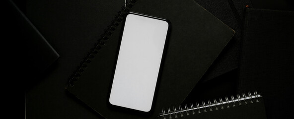 Blank screen smartphone above black notebook on dark modern worktable