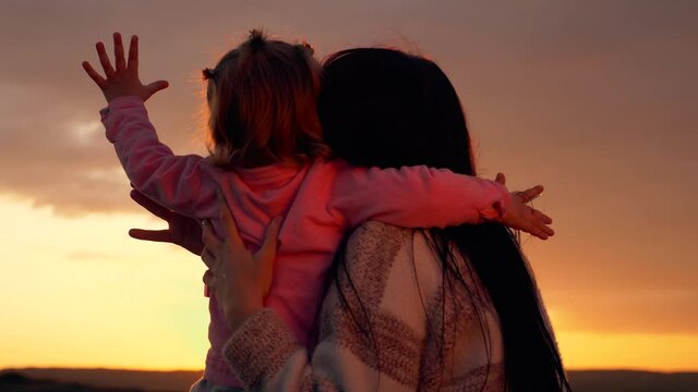 A young mother with a small child in the Park at sunset. The daughter puts her arms around her mother's neck. A happy family enjoys a beautiful sunset.