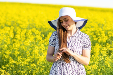 Beautiful girl in a rapeseed field, in a dress and hat.