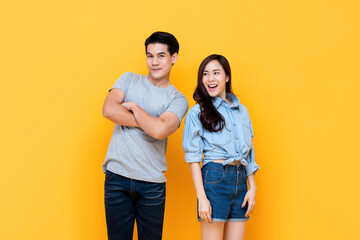 Fototapeta premium Timid smiling young Asian couple trying to be closer to each other isolated on yellow studio background