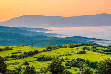 bright green meadow on a background of mountains in the fog. Sunrise. The beginning of the day.