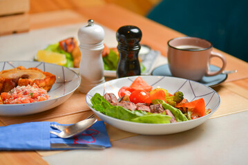 Salad with meat and vegetables. Italian cuisine, different dishes served in restaurant on light rustic wooden table.