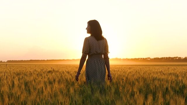 A girl in a dress walks through a wheat field, touching the spikelets of wheat, inspired by nature and a beautiful sunset.