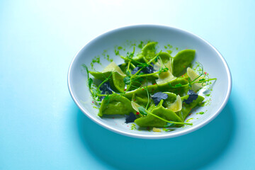 Green spinach ravioli dumplings with ricotta cheese and meat filling served in a blue plate over pastel blue background.