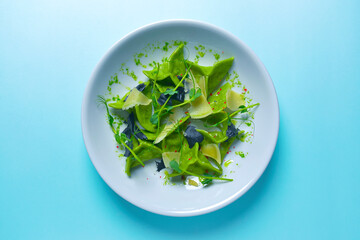 Green spinach ravioli dumplings with ricotta cheese and meat filling served in a blue plate over pastel blue background.