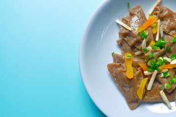 Buckwheat dumplings with greenery served on a plate over blue background. Tasty dish isolated on blue.