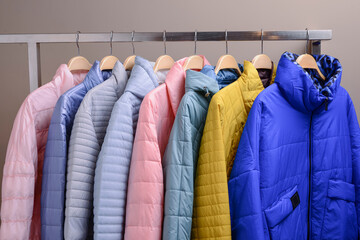 New collection of down jackets on hangers in the market. Colorful background of modern spring, autumn outerwear.