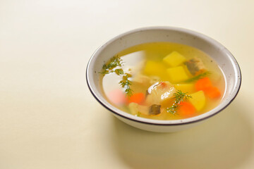 Delicious stew soup with meat and vegetables served in a white bowl over bright pastel yellow background. Healthy diet.