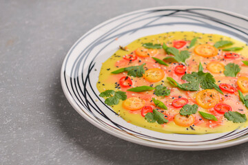 Chilled cucumber avocado soup with salmon fish, tomato, pepper, fresh greenery served in a plate over gray background.
