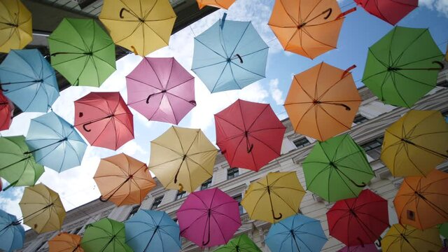 Colorful Umbrellas Hanging in the Air above the Street. Low angle rotating view