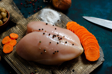 fresh chicken breast on a wooden board with raw carrots and spices