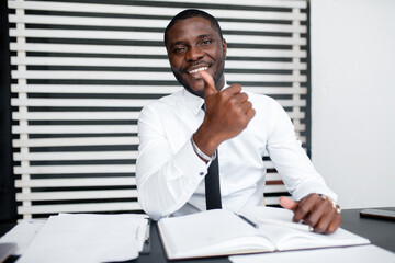 Black business executive in white shirt smiles and shows thumb up sitting at a table in the office