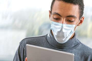 view of a afro-american young man with aCovid 19 proctection mask having an online consultation with his doctor