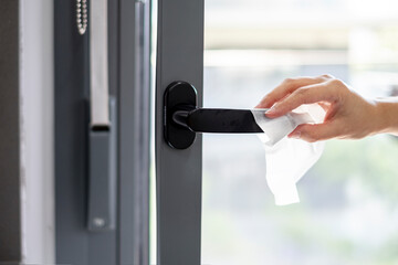 woman cleaning the doorknob with an alcohol disinfecting antibacterial wipe as a prevention to kill...