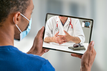 view of a afro-american young man with aCovid 19 proctection mask having an online consultation with his doctor