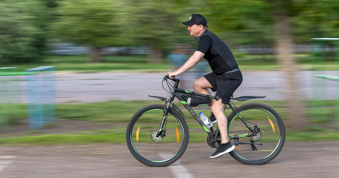 Sterlitamak, Republic of Bashkortostan, Russia - June 10, 2020. Training at the school stadium. A cyclist rushes at breakneck speed against a background of green trees.