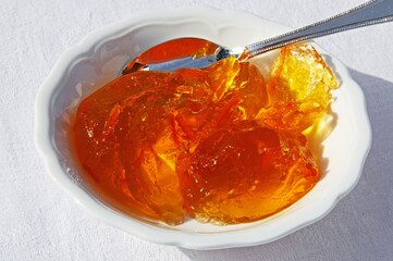 Orange marmalade in a white ceramic dish with a silver spoon.