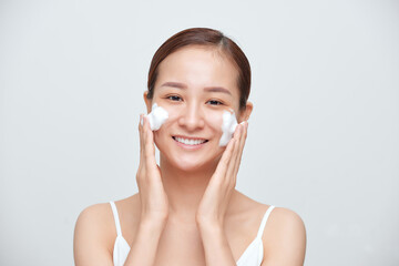 Portrait of young Asian woman applying foaming cleanser against white background.