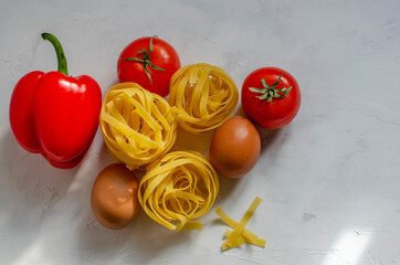 Fototapeta na wymiar raw tagliatelle pasta with eggs, tomatoes and bell peppers on the table