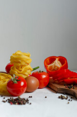 raw tagliatelle pasta with eggs, tomatoes and bell peppers on the table