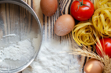 raw tagliatelle pasta with eggs, tomatoes and bell peppers on the table