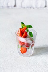 Water with ice, strawberry syrup, fresh strawberries and mint in a glass cup on a white background. A refreshing strawberry drink.