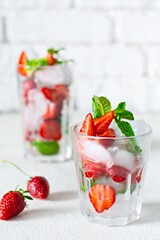 Water with ice, strawberry syrup, fresh strawberries and mint in a glass cup on a white background. A refreshing strawberry drink.