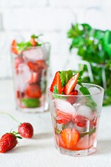 Water with ice, strawberry syrup, fresh strawberries and mint in a glass cup on a white background. A refreshing strawberry drink.