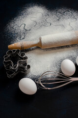 ingredients for cookies. cookie cutters on a dark background with flour and a rolling pin