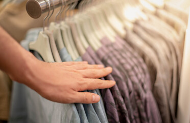 Naklejka premium Male hand choosing clothes for checked pattern cotton shirt on the rack in cloth shop at department store.