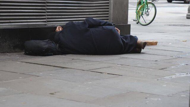 A homeless man sleeping beside the corner of a building.