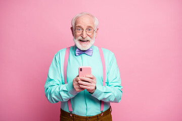 Portrait of positive cheerful old man blogger use cellphone comment social media news repost share wear teal turquoise shirt purple violet bow tie isolated pastel pink color background