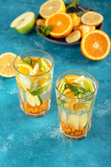 vertical homemade lemonade with lemon, orange, sea buckthorn and mint in glasses on blue background, summer drink concept