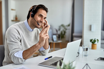 Happy businessman communicating via headset while working on laptop at home.