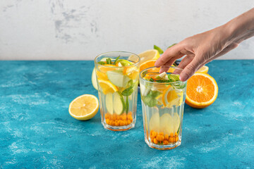 refreshing detox water with lemon, orange, mint in glasses wiht hand on white blue background, summer homemade lemonade