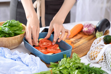 process of cooking vegetables with hands, tomatoes placed in baking dish, vegetarian dinner